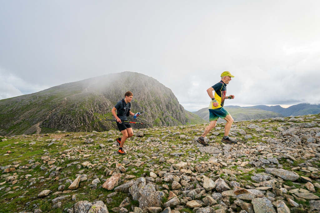 Running hard over Green Gable with Great Gable in the background and support runner Matt carrying poles and fluid